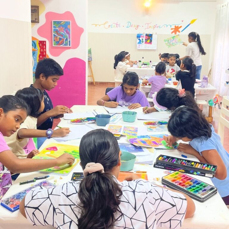 Kids painting and drawing at tables in the Art Club studio, with finished artwork pinned to the wall behind them