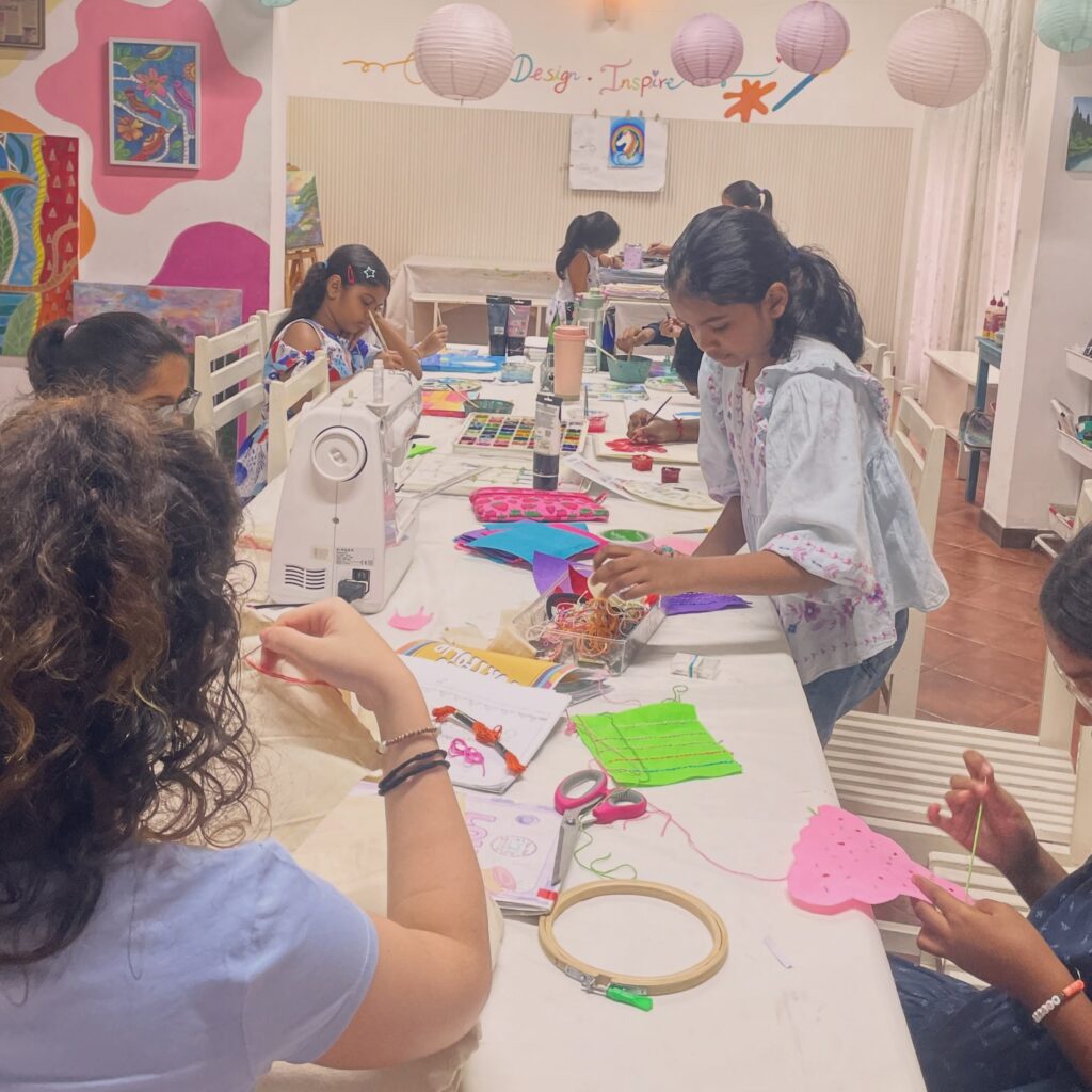 Wide view of a busy studio class, with kids painting, sewing machines, and an embroidery hoop on the table