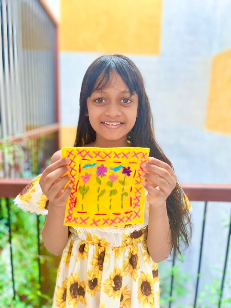 A girl in a sunflower dress holding her embroidered yellow felt patch